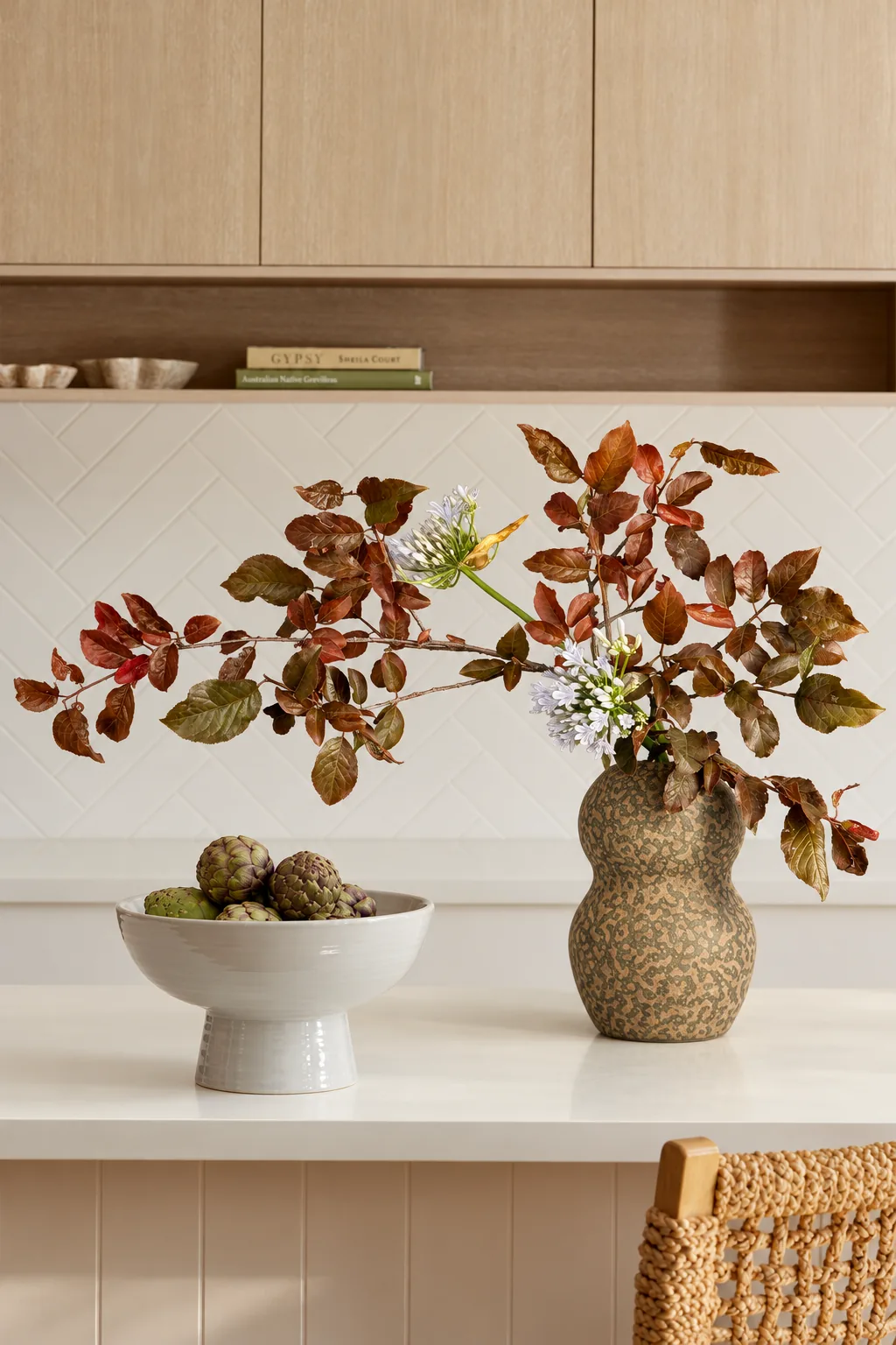 Composition with rust-coloured autumn branches and small pale blue flowers in a double-gourd vase on a kitchen counter