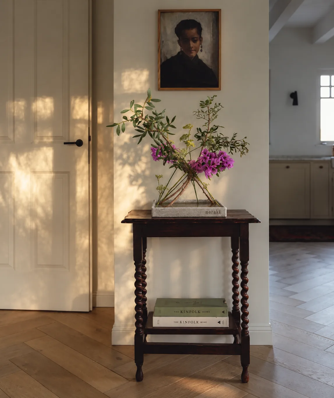 Composition with purple flowers and green branches in a stone tray on a small wooden table by a door